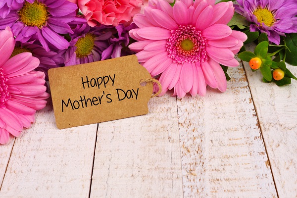 Happy Mothers Day tag close up among a bouquet of flowers over a white wood background