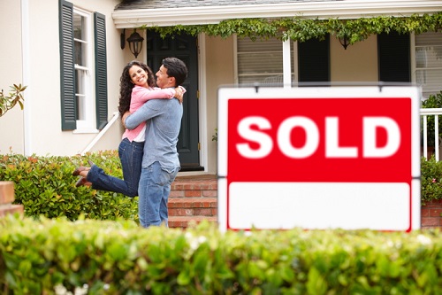 Hispanic couple outside home with sold sign